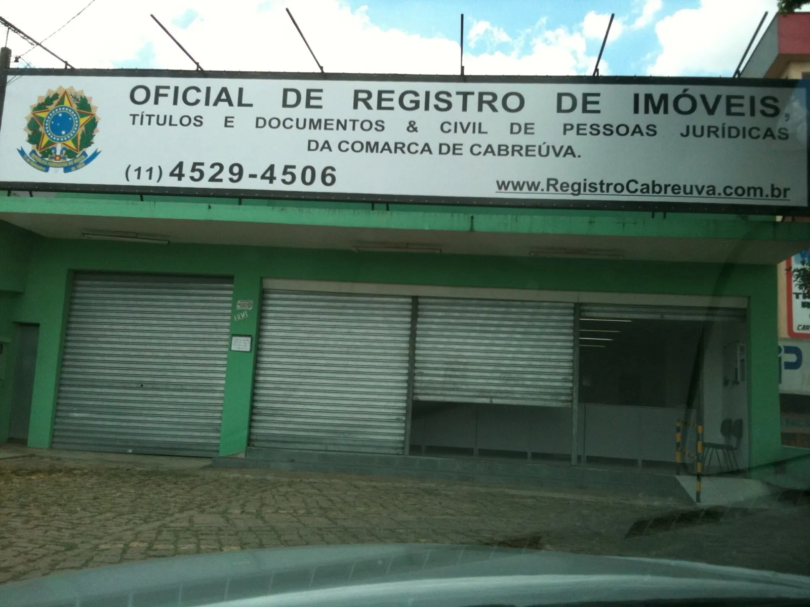 Fachada verde de cartório com placa 'Oficial de Registro de Imóveis' em Cabreúva, interior de São Paulo, com portas de aço fechadas