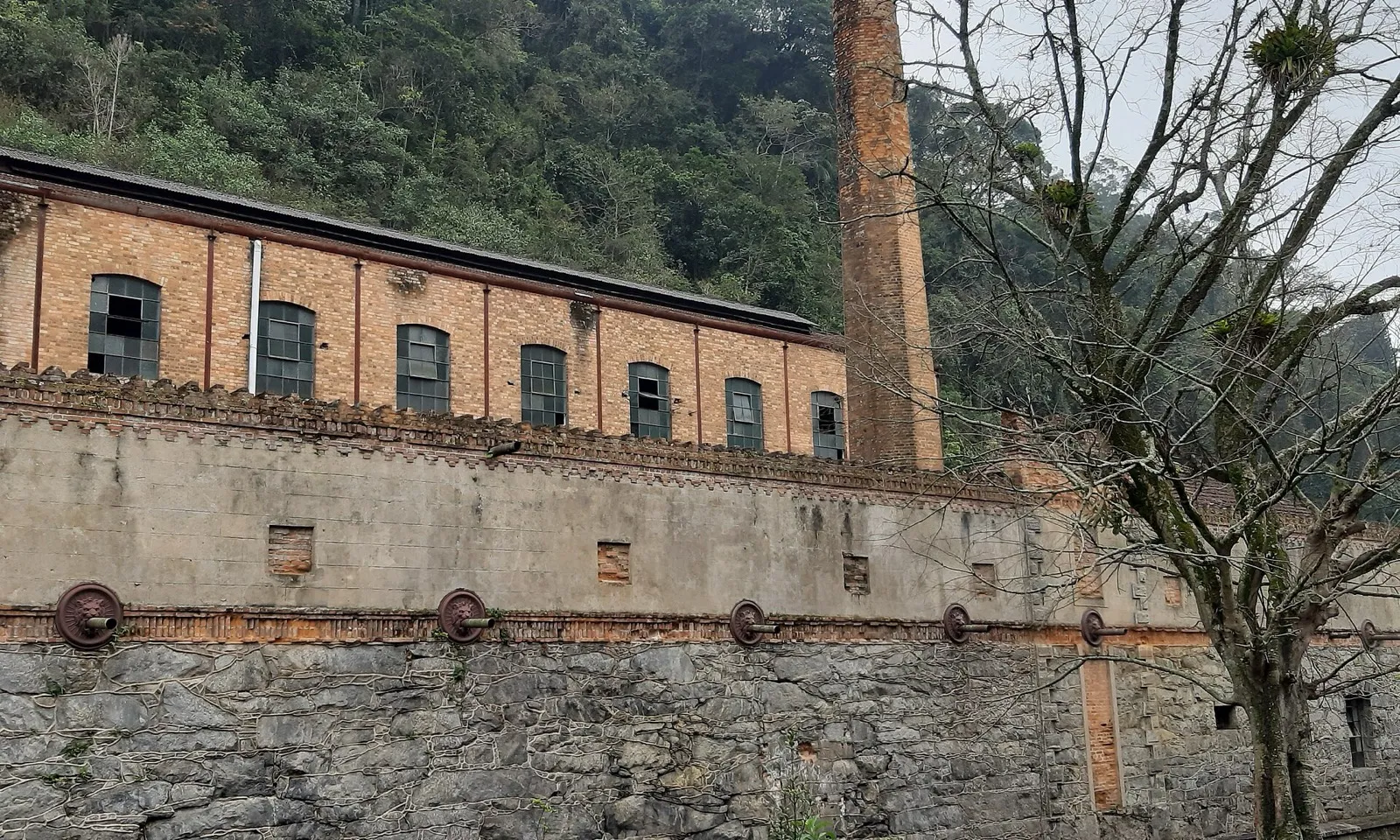 Prédio antigo de fábrica de tecidos com janelas quebradas e chaminé de tijolos