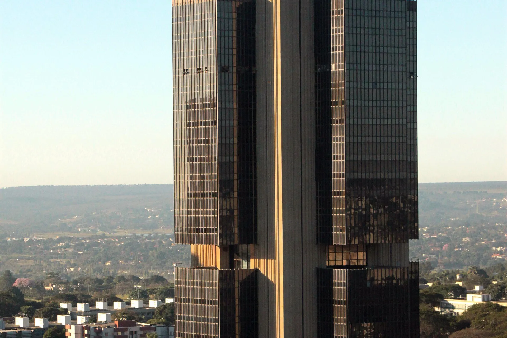 Torre de vidro escuro e faixa central de concreto do Edifício-Sede do Banco Central, em Brasília, sob céu claro, com a cidade ao fundo