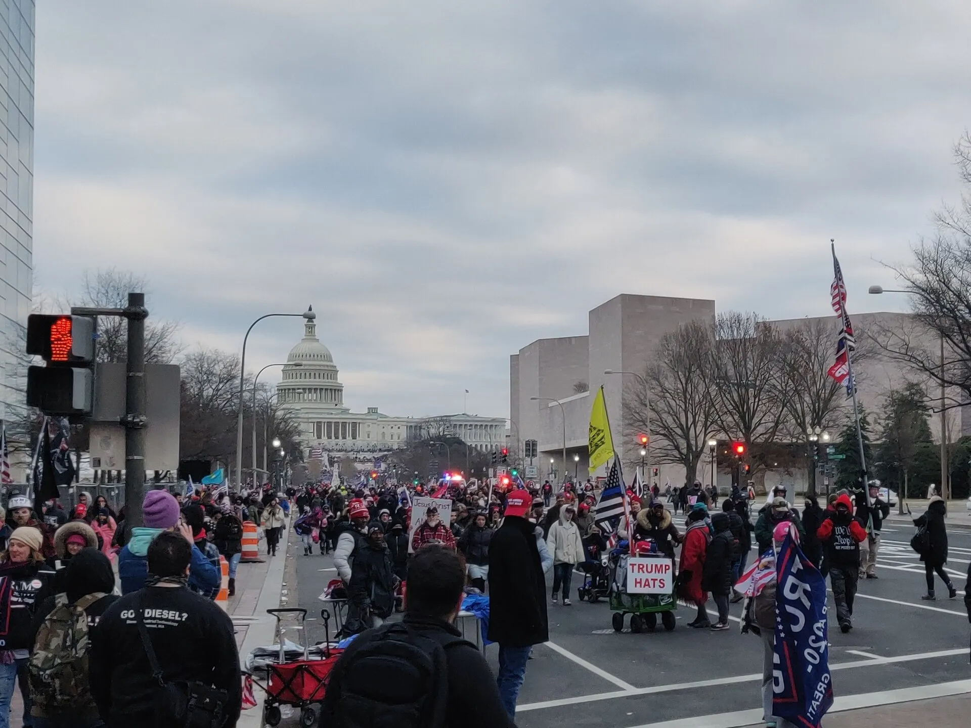 Multidão de apoiadores de Donald Trump caminha por uma avenida em Washington, com a cúpula do Capitólio ao fundo, em dia nublado