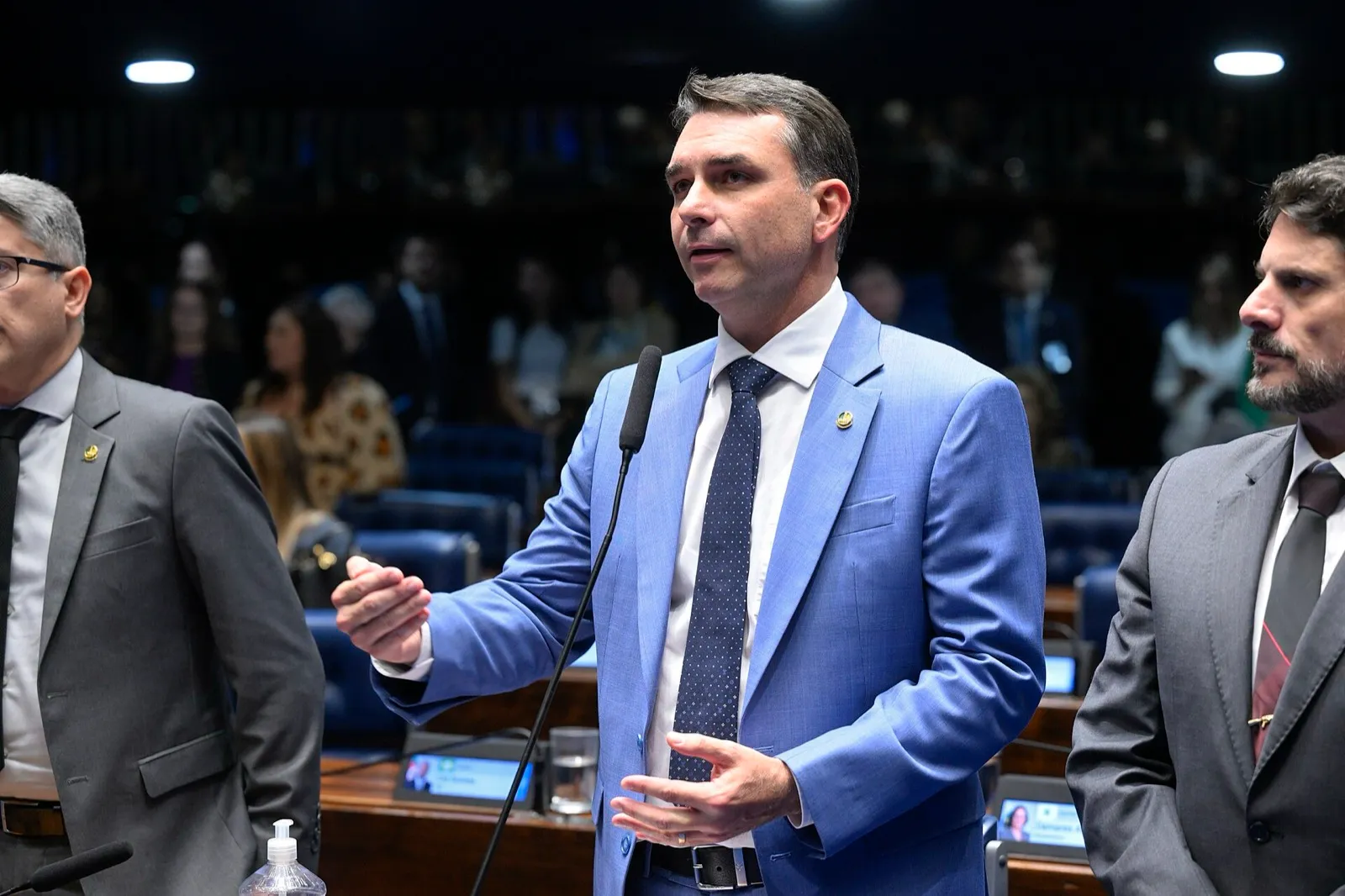 Flávio Bolsonaro fala ao microfone no plenário do Senado, entre outros parlamentares