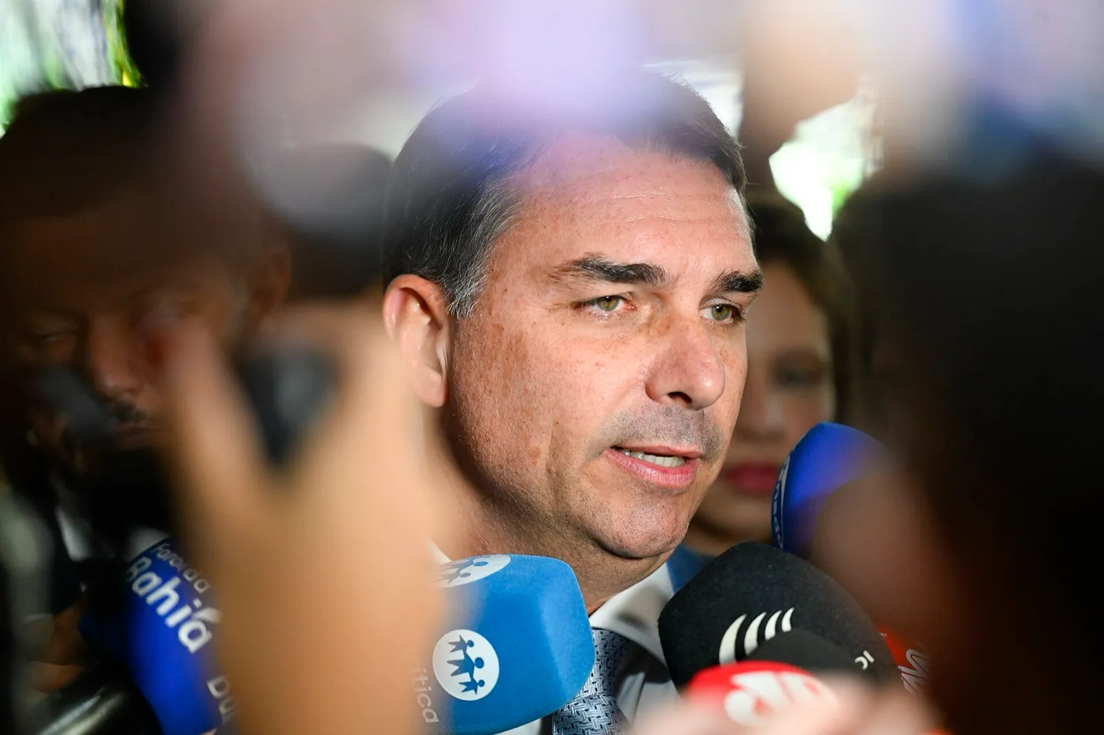Senador Flávio Bolsonaro fala a jornalistas, com vários microfones à sua frente