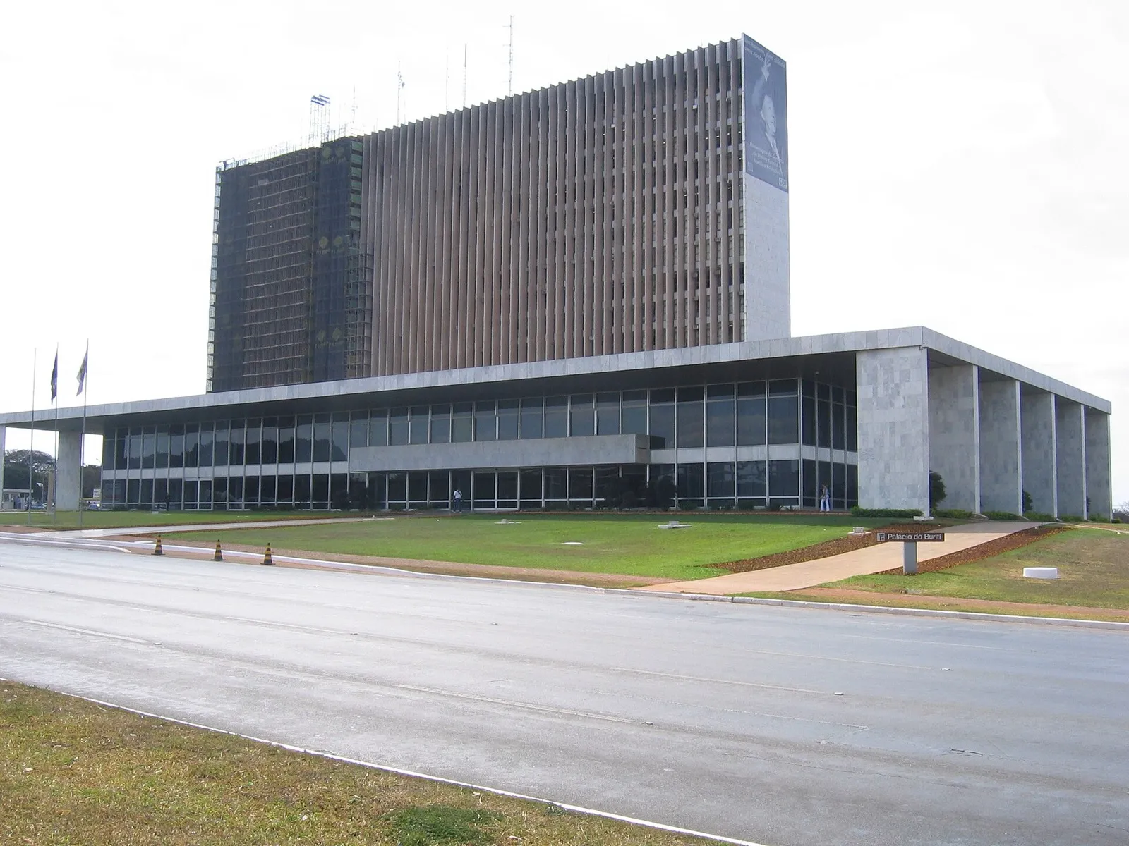 Fachada do Palácio do Buriti, em Brasília, com colunas de mármore, janelas de vidro e um prédio alto ao fundo