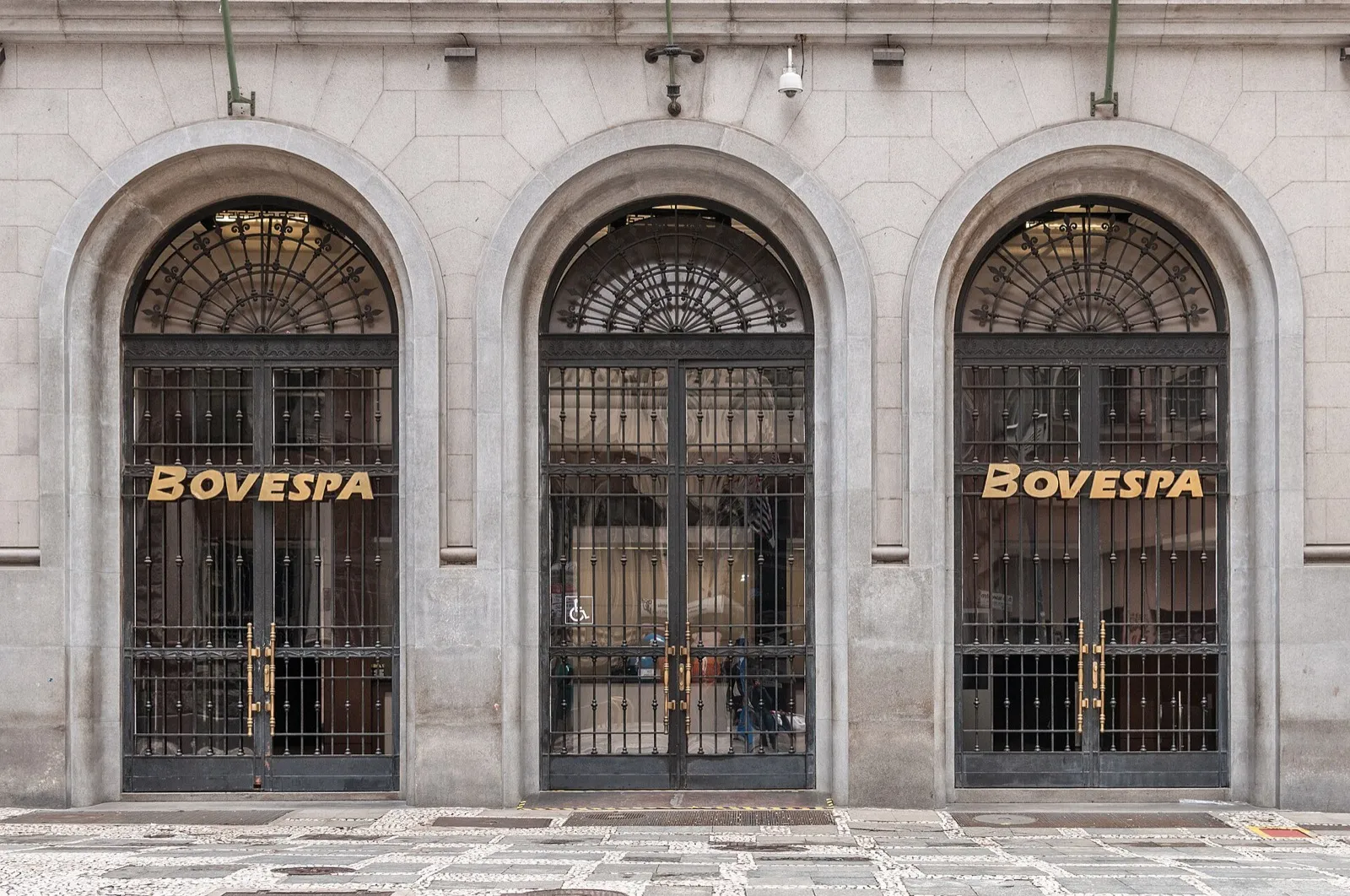 Fachada de pedra do prédio da Bovespa, com três portões de ferro e letras douradas com o nome Bovespa