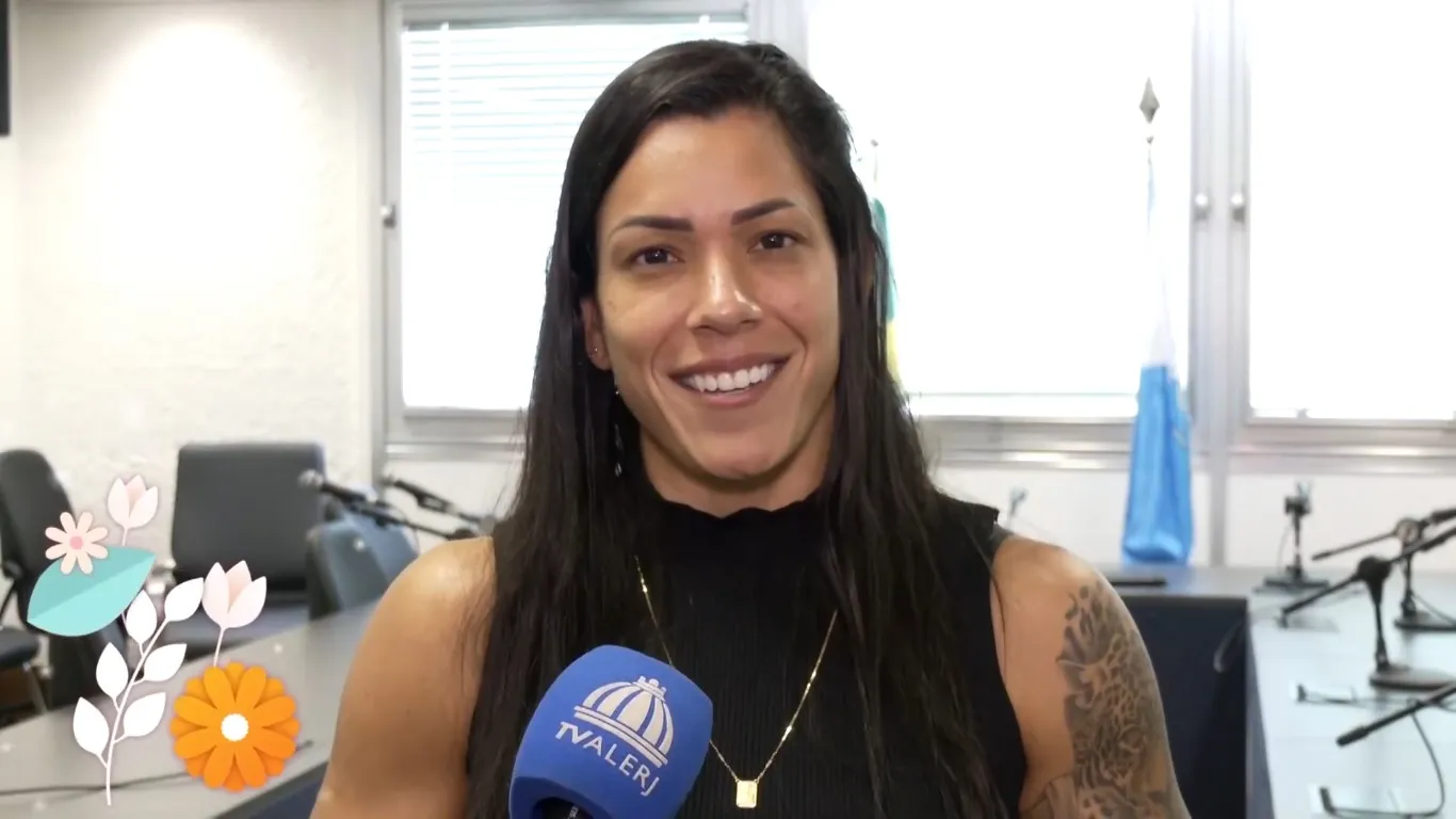 Índia Armelau sorri durante entrevista e segura microfone da TV Alerj