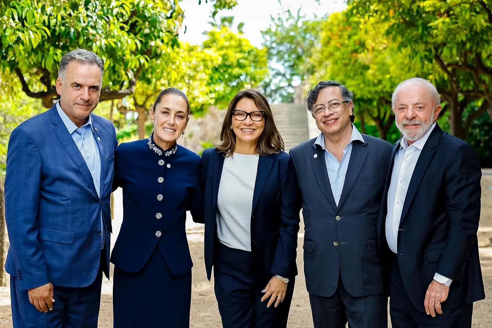Cinco pessoas sorriem ao ar livre, sob árvores. Claudia Sheinbaum é a segunda da esquerda para a direita, e Lula é o último à direita.