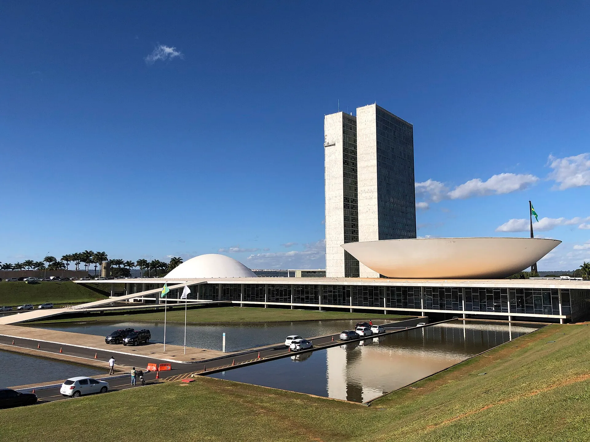 Fachada do Congresso Nacional, em Brasília, com as duas torres, as cúpulas e os espelhos d'água sob céu azul